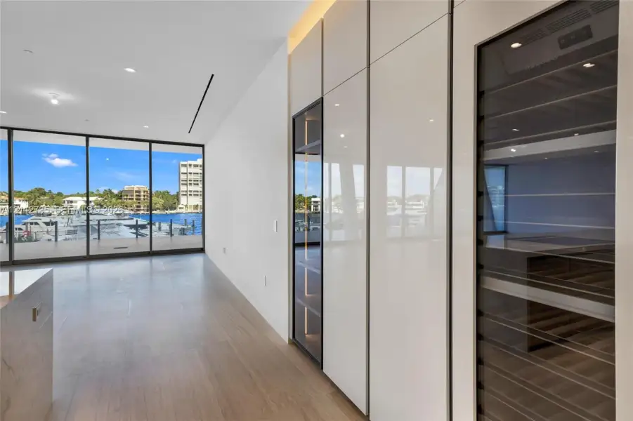 Floor-to-ceiling glass wall, custom cabinetry with high-gloss finish, integrated wine refrigeration, and wood-finish flooring