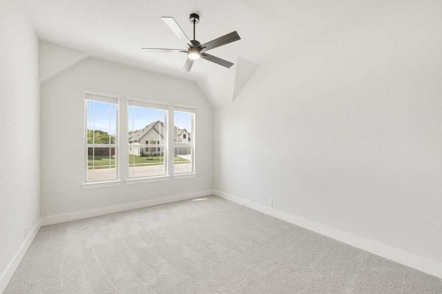 Empty bedroom with vaulted ceiling, ceiling fan, carpet flooring, and triple windows overlooking neighborhood
