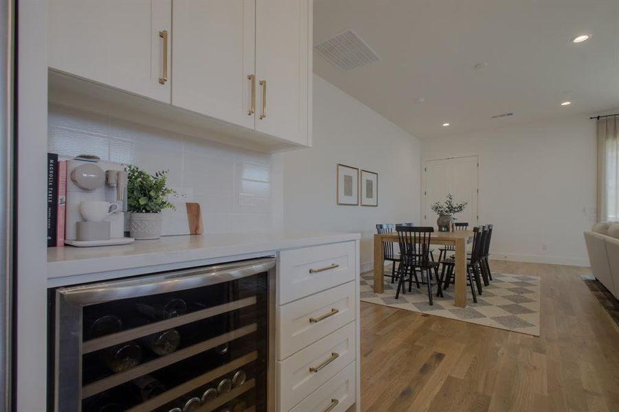 Kitchen with backsplash, white cabinetry, beverage cooler, and wood-type flooring