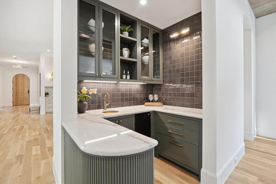 The wet bar with brass fixtures and sink, ice maker, glass cabinetry, counter to ceiling tile and reeded details. No details were missed in showcasing this space!