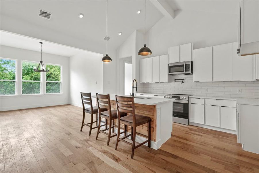 Kitchen with stainless steel appliances, light countertops, backsplash, beam ceiling, and a kitchen island with sink