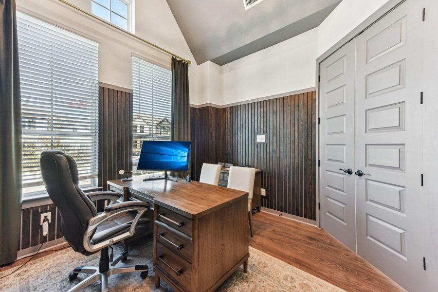 A spacious home office showcases vaulted ceilings, wood wainscoting, and rich hardwood flooring.
