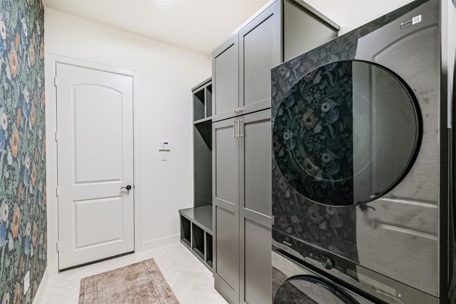 Spacious mudroom/laundry with dark cabinetry, floral wallpaper accent, and stacked washer/dryer.