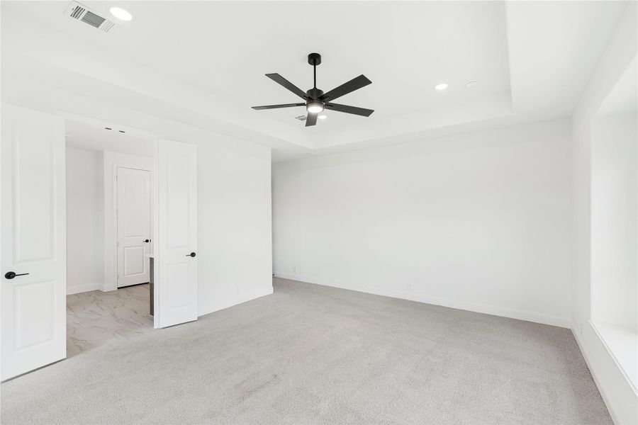Empty bedroom with tray ceiling, black ceiling fan, gray carpet, and white walls