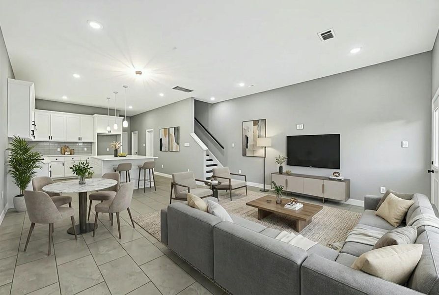 This photo showcases a modern open-concept living area with a spacious layout. It features a sleek kitchen with white cabinetry and a breakfast bar, a staged cozy dining area, and a comfortable living room with a large sectional sofa and wall-mounted TV. Neutral tones and ample lighting create a bright, inviting atmosphere.