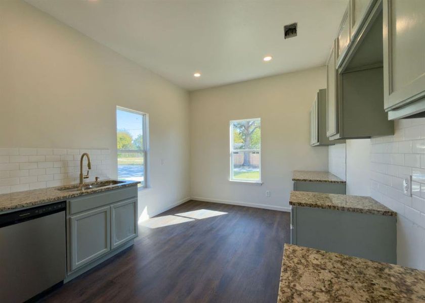 Kitchen featuring backsplash, stainless steel dishwasher, light stone countertops, dark wood-type flooring, and recessed lighting Kitchen featuring backsplash, stainless steel dishwasher, light stone countertops, dark wood-type flooring, and recessed lighting