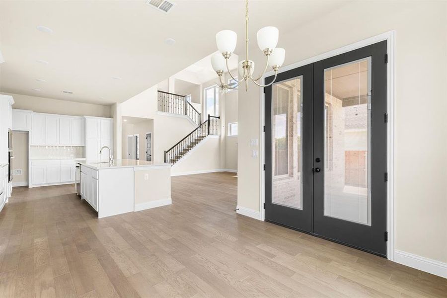 Kitchen featuring an inviting chandelier, white cabinetry, french doors, and a center island with sink