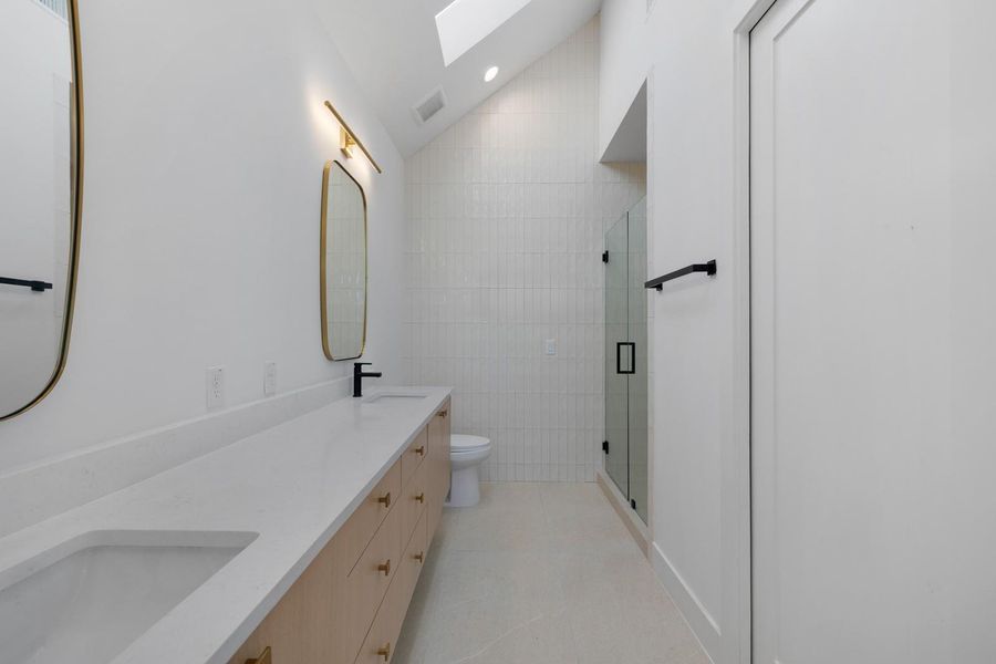 Bathroom featuring lofted ceiling, a stall shower, double vanity, a skylight, and tile walls Bathroom featuring lofted ceiling, a stall shower, double vanity, a skylight, and tile walls