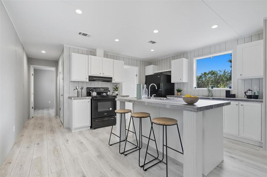 Kitchen with black appliances, white cabinets, a kitchen breakfast bar, recessed lighting, and an island with sink Kitchen with black appliances, white cabinets, a kitchen breakfast bar, recessed lighting, and an island with sink