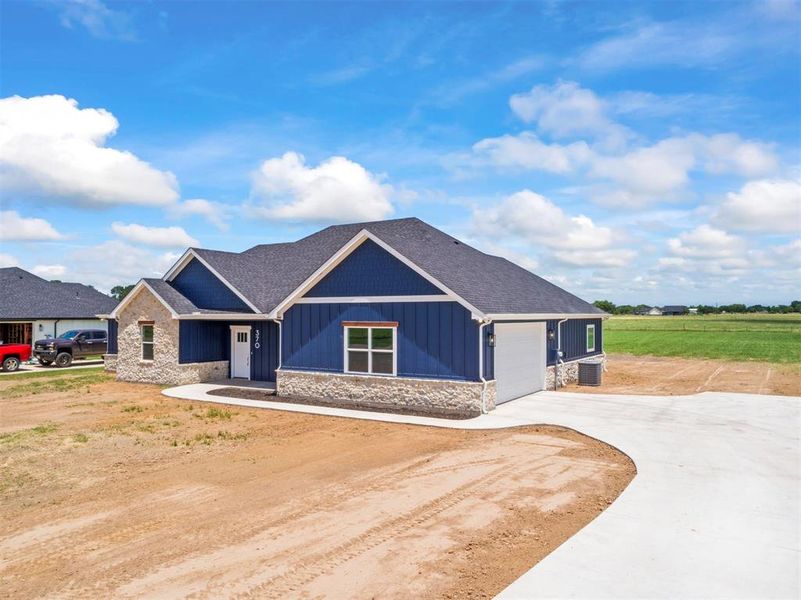 View of front of house featuring stone siding, driveway, an attached garage, board and batten siding, and roof with shingles