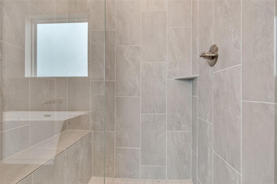 Indulge in this well-appointed shower space, featuring a built-in bench and elegant tiled walls.