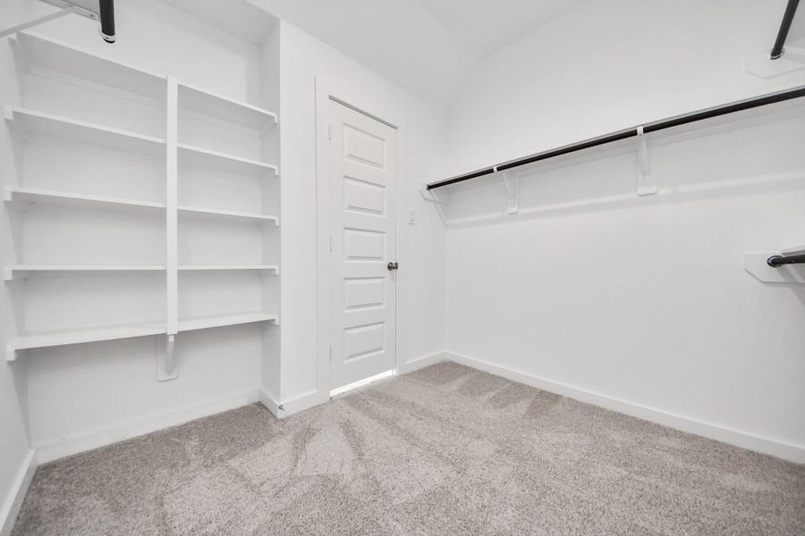 Walk-in closet that epitomizes luxury and practicality. This generously sized space features built-in shelving, offering abundant room for impeccable organization. High ceilings and recessed lighting create a bright and welcoming ambiance. Sample photo of completed home with similar floor plan. Actual colors and selections may vary.