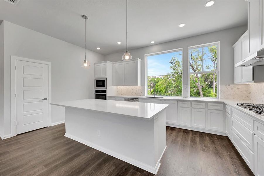 Modern kitchen featuring an expansive island, white cabinetry, integrated stainless steel appliances, and wood-finish flooring
