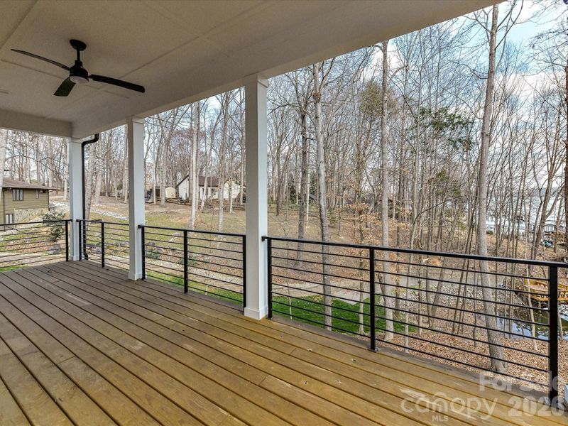 Lakefront covered deck with modern cable railing and ceiling fan, offering peaceful wooded views and the perfect setting to relax and enjoy waterfront living.