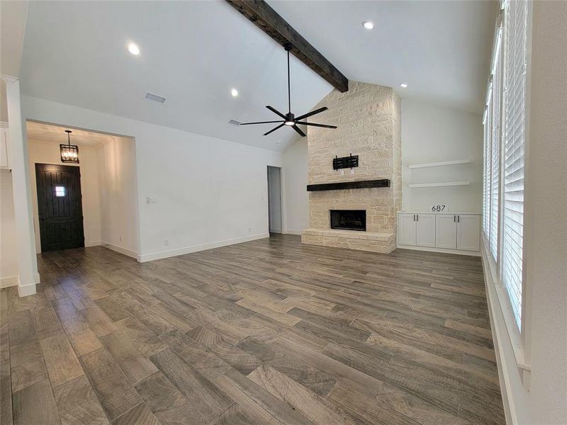 Unfurnished living room featuring ceiling fan with notable chandelier, lofted ceiling with beams, and a stone fireplace