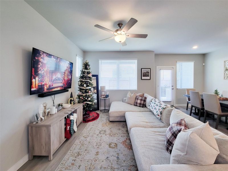 This inviting living space features a room well-lit with natural light from multiple windows, and a ceiling fan adds comfort. Open layout seamlessly connects to the dining area, perfect for entertaining.