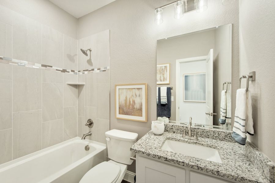 Bathroom with granite countertop vanity, tiled shower-tub combo, and large mirror with overhead lighting