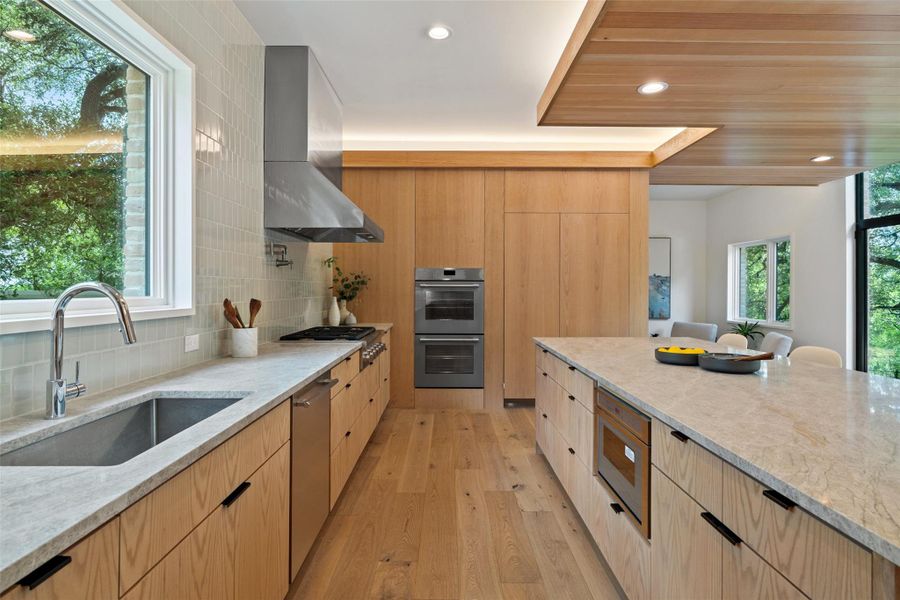 Kitchen with light stone countertops, light wood finished floors, recessed lighting, modern cabinets, and backsplash