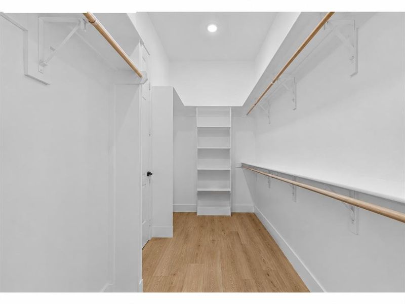 Walk-in closet featuring light wood-finish flooring, white walls, built-in shelving, and dual hanging rods Walk-in closet featuring light wood-finish flooring, white walls, built-in shelving, and dual hanging rods