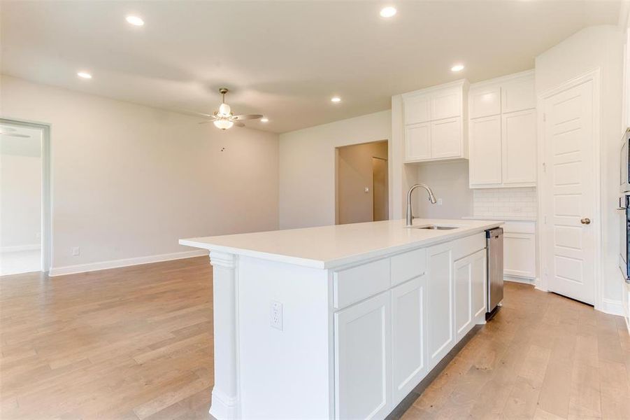 Kitchen featuring white cabinets, decorative backsplash, light wood-type flooring, an island with sink, and ceiling fan