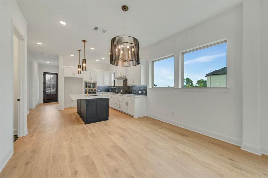 Open-concept living space featuring wood-finish flooring, a modern kitchen with a dark-toned island, pendant lighting, built-in appliances, and multiple windows