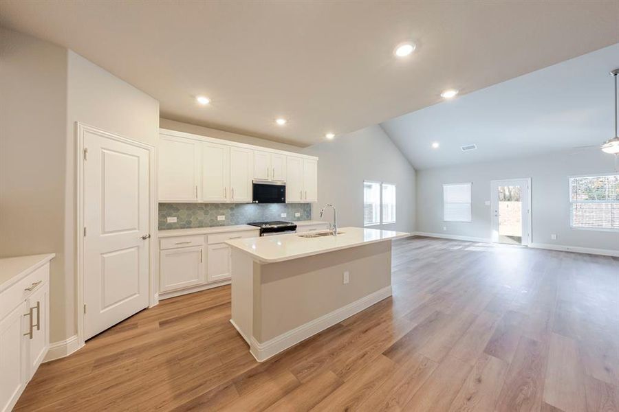 Kitchen with a center island with sink, lofted ceiling, white cabinetry, light wood-style flooring, and open floor plan Kitchen with a center island with sink, lofted ceiling, white cabinetry, light wood-style flooring, and open floor plan