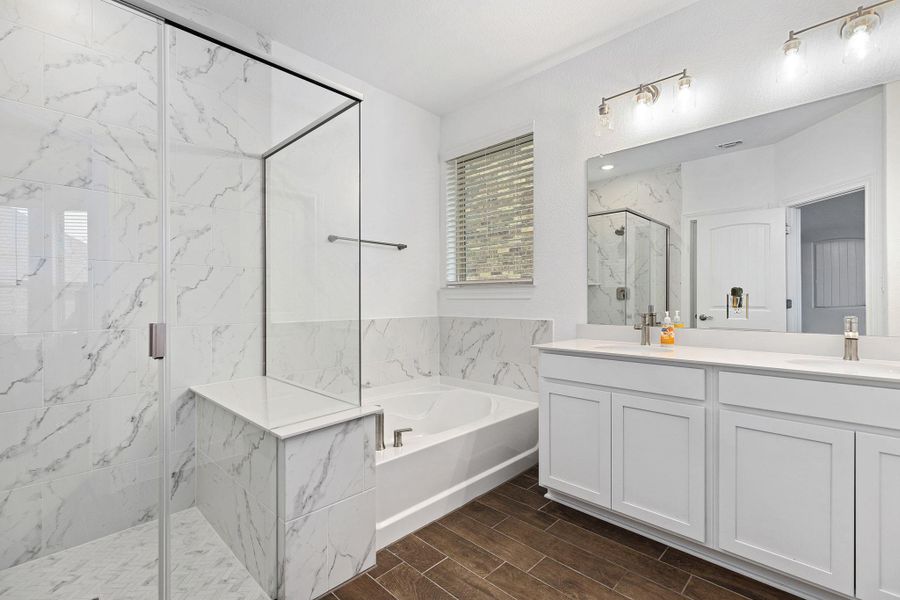 Marble-look tile and wood-look flooring enhance this primary bathroom, featuring a dual vanity and glass-enclosed shower.
