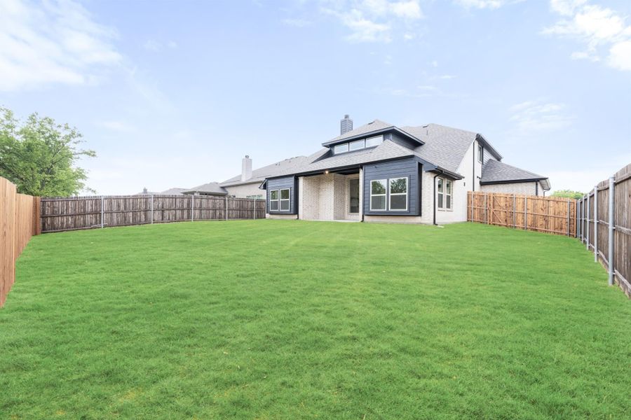 Backyard with large green lawn, wood privacy fence, and rear view of two-story brick and blue siding home