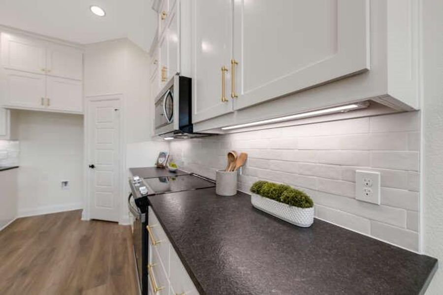 Kitchen featuring electric range oven, white cabinets, tasteful backsplash, dark countertops, and stainless steel microwave Kitchen featuring electric range oven, white cabinets, tasteful backsplash, dark countertops, and stainless steel microwave