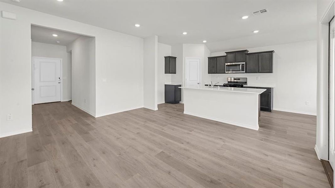 Kitchen featuring a kitchen island with sink, recessed lighting, appliances with stainless steel finishes, light wood-type flooring, and dark cabinetry
