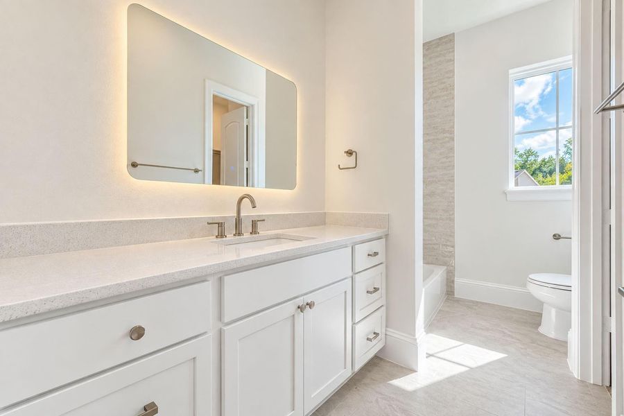 Beautifully finished secondary bath featuring an extended vanity with generous cabinetry, quartz countertops, sleek fixtures, and a statement illuminated mirror. A glass-enclosed shower and natural light complete the fresh, sophisticated design, creating a polished retreat for family or guests. Beautifully finished secondary bath featuring an extended vanity with generous cabinetry, quartz countertops, sleek fixtures, and a statement illuminated mirror. A glass-enclosed shower and natural light complete the fresh, sophisticated design, creating a polished retreat for family or guests.