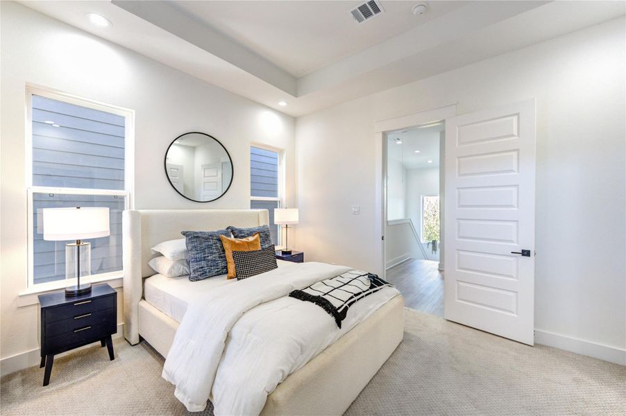 Primary bedroom located on the third floor featuring 10-ft coffered ceilings, a private ensuite balcony, and dual walk-in closets with box shelving. Pre-wired for a ceiling fan and 5.1 surround sound, with carpeted flooring and a private ensuite bathroom.