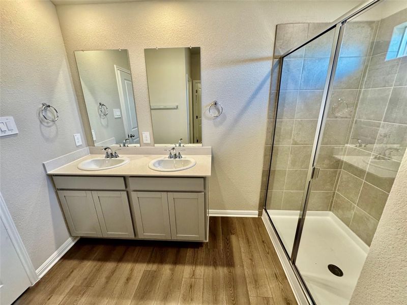 Full bath with wood finished floors, a stall shower, double vanity, and a textured wall