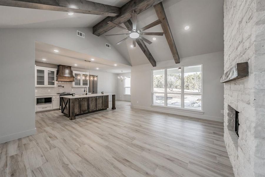 Unfurnished living room with ceiling fan, a stone fireplace, a chandelier, recessed lighting, and beamed ceiling