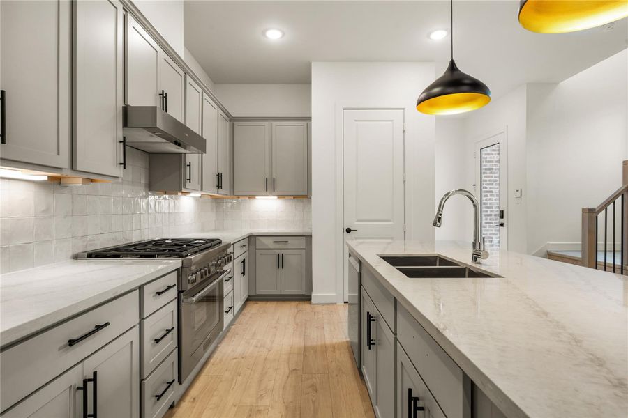 Cooking wall detail — professional gas range, stainless steel vent hood, under-cabinet accent illumination, and square zellige-style tile backsplash.
