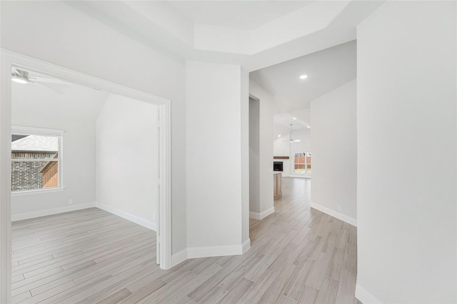 Empty hallway with light wood-look floors, tray ceiling, and open view to kitchen beyond