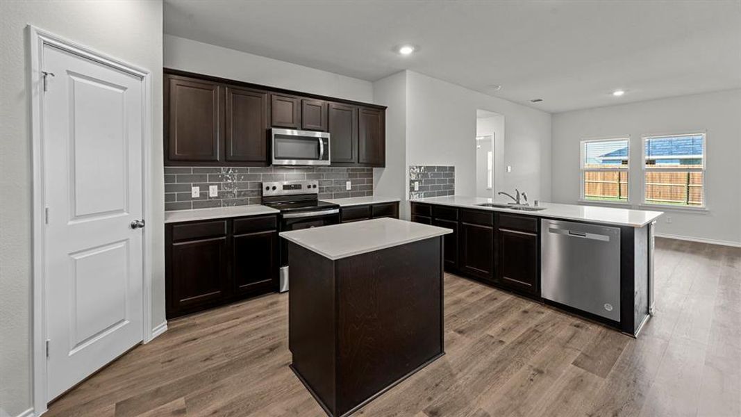 Kitchen featuring a peninsula, stainless steel appliances, dark wood finish cabinets, a center island, and tasteful backsplash