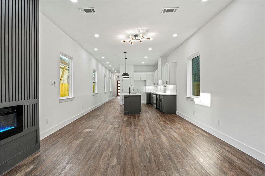 Kitchen featuring a kitchen island with sink, open floor plan, white cabinetry, dark wood finished floors, and light countertops