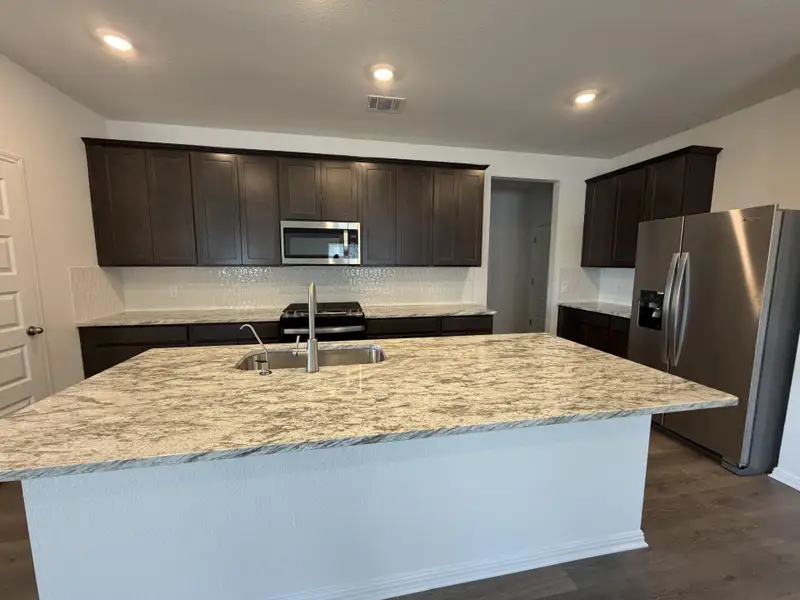 Kitchen featuring dark wood-style floors, stainless steel appliances, dark brown cabinets, backsplash, and light stone counters Kitchen featuring dark wood-style floors, stainless steel appliances, dark brown cabinets, backsplash, and light stone counters