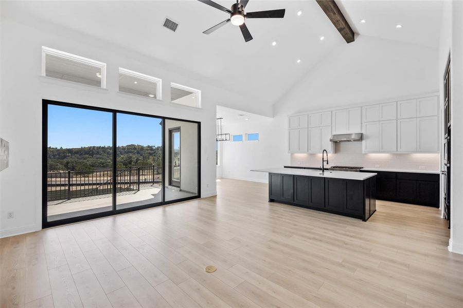 Two tone kitchen featuring ceiling fan, dual tone cabinets, a center island with sink, open floor plan, and backsplash