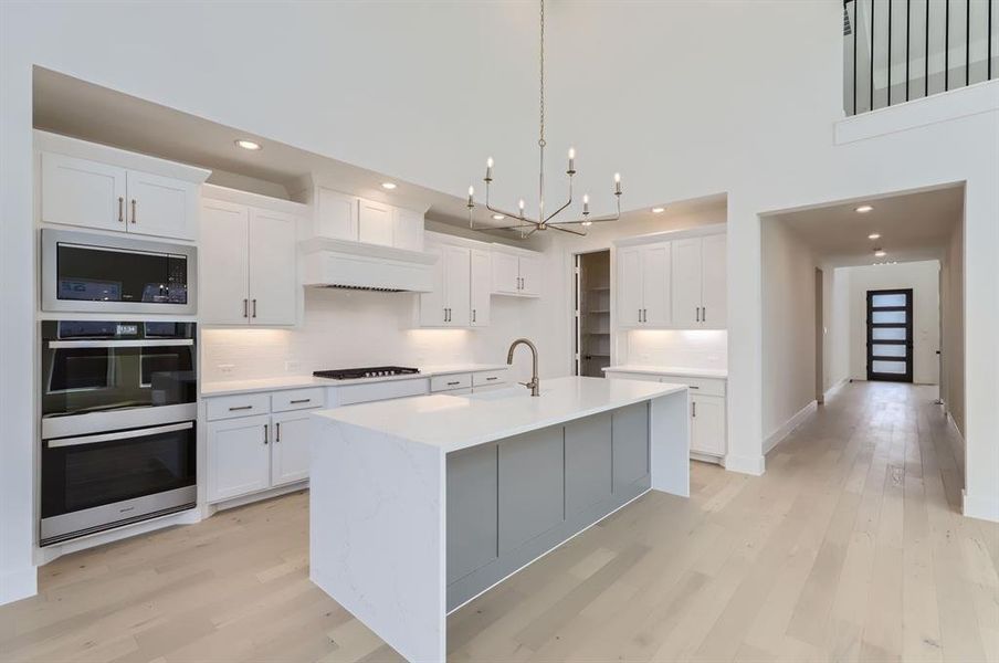 Kitchen featuring a towering ceiling, white cabinets, a kitchen island with sink, and hanging light fixtures