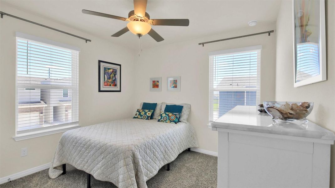 Bedroom featuring a ceiling fan with integrated lighting, two windows with blinds, and neutral carpeting