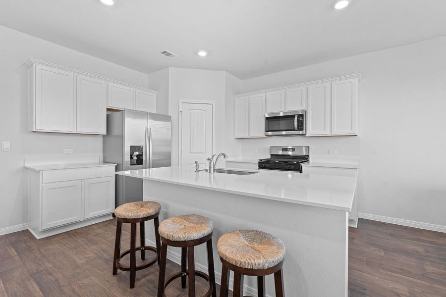 Kitchen with white cabinetry, dark wood finished floors, stainless steel appliances, a center island with sink, and recessed lighting Kitchen with white cabinetry, dark wood finished floors, stainless steel appliances, a center island with sink, and recessed lighting