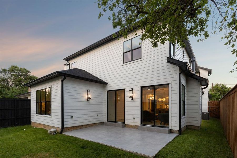 Back house at dusk featuring a yard and a patio