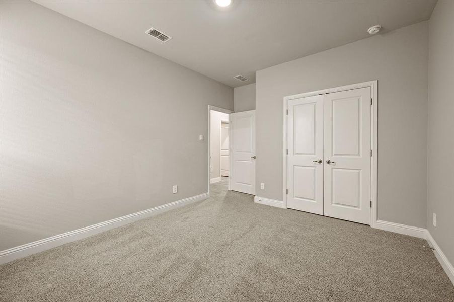 Spacious secondary bedroom featuring soft carpet, neutral paint tones, and a large closet with double doors for ample storage.
