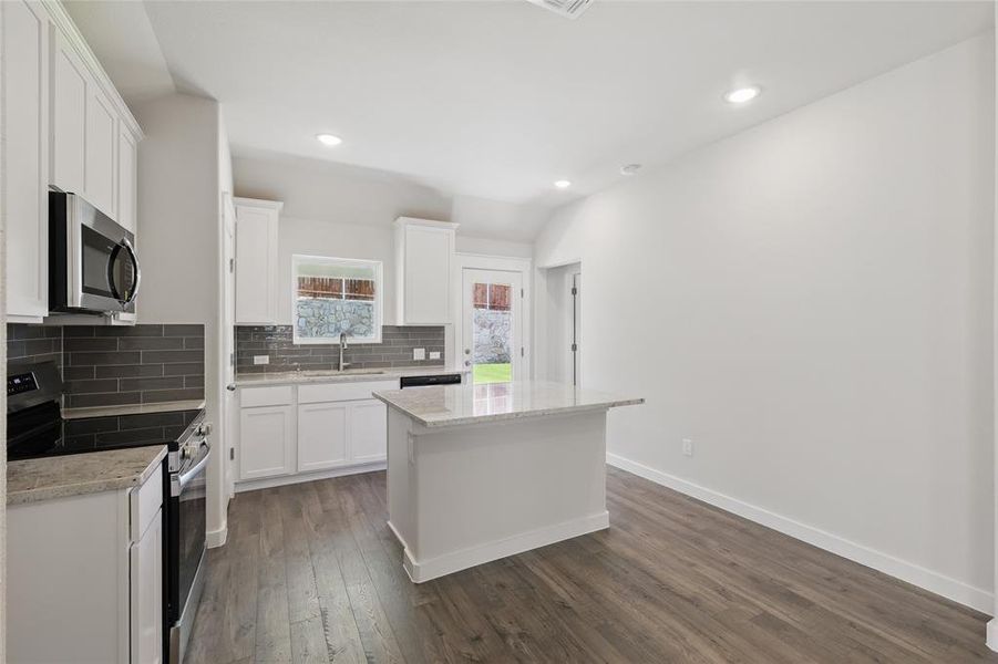 Kitchen with appliances with stainless steel finishes, backsplash, dark wood-style floors, white cabinets, and recessed lighting Kitchen with appliances with stainless steel finishes, backsplash, dark wood-style floors, white cabinets, and recessed lighting
