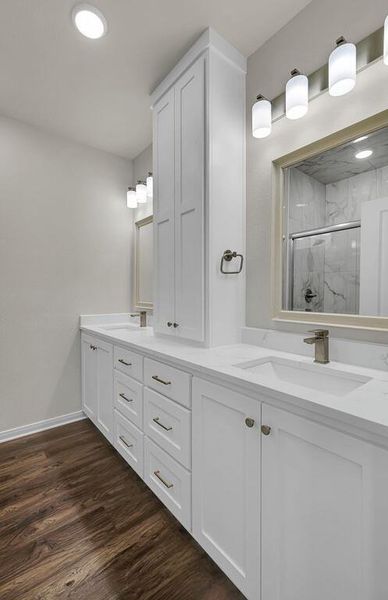 Bathroom featuring a marble finish shower, double vanity, and wood finished floors
