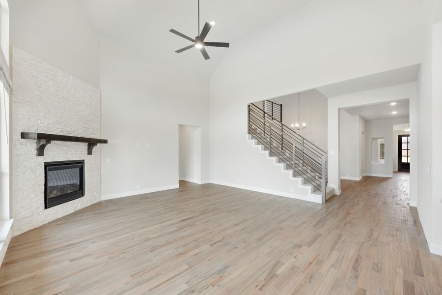 Open living room with vaulted ceiling, stone fireplace, hardwood floors, and staircase with metal railing Open living room with vaulted ceiling, stone fireplace, hardwood floors, and staircase with metal railing