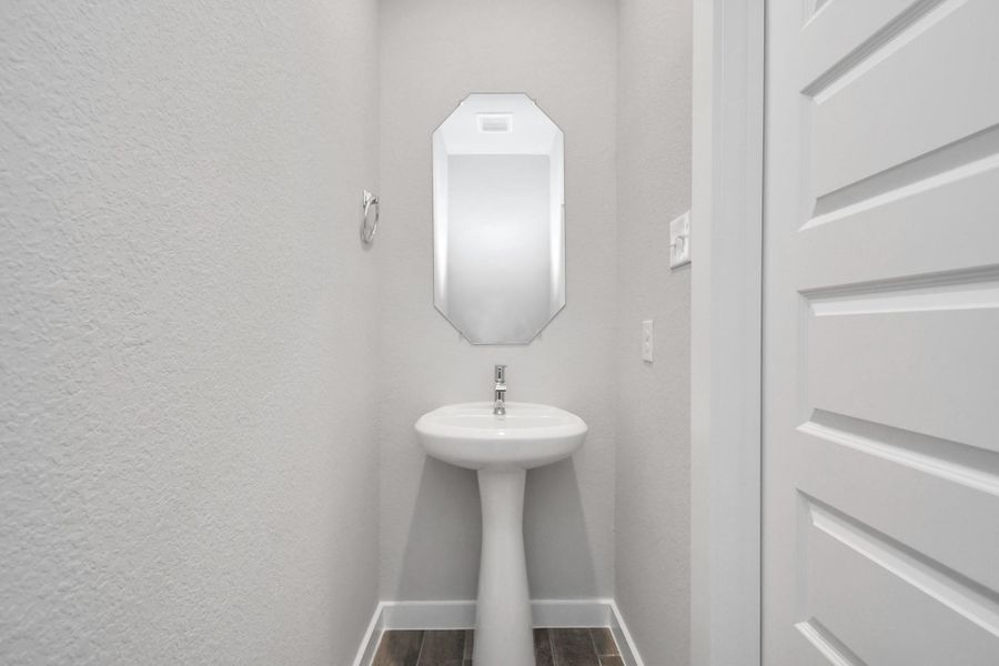 Step into this bright and airy half bath, where a sleek pedestal sink and modern hardware elevate the space with contemporary charm. Sample photo of completed home with similar floor plan. Actual colors and selections may vary.