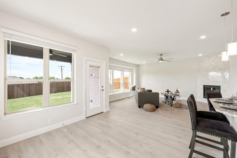 Open-plan living and dining area with light wood floors, ceiling fan, and large windows overlooking a fenced backyard.